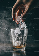 Hand Adding Ice Cubes to Whiskey Glass with Splash