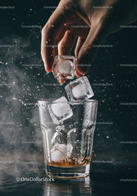 Hand Adding Ice Cubes to Whiskey Glass with Splash