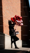 Man holding heart-shaped balloons and chocolates outdoors