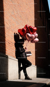 Man holding heart-shaped balloons and chocolates outdoors