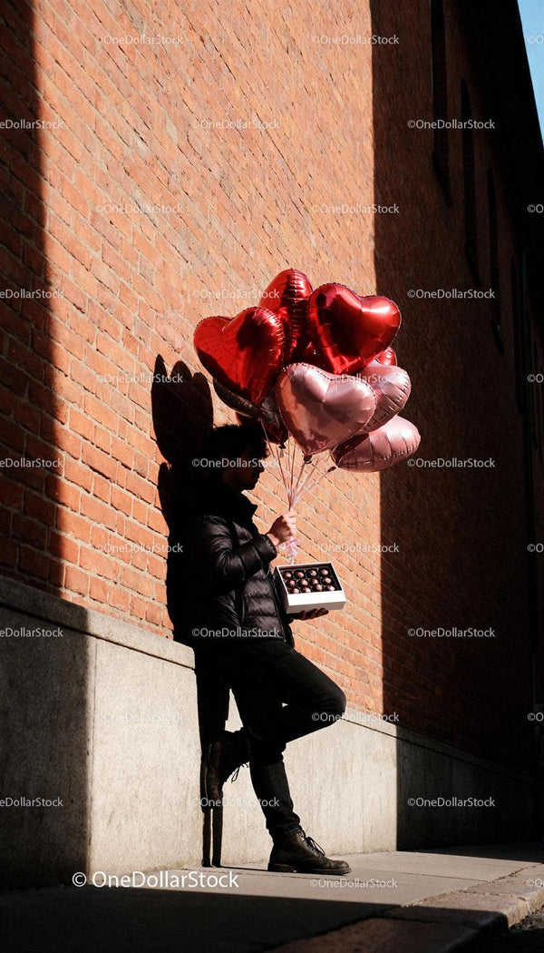 Man holding heart-shaped balloons and chocolates outdoors