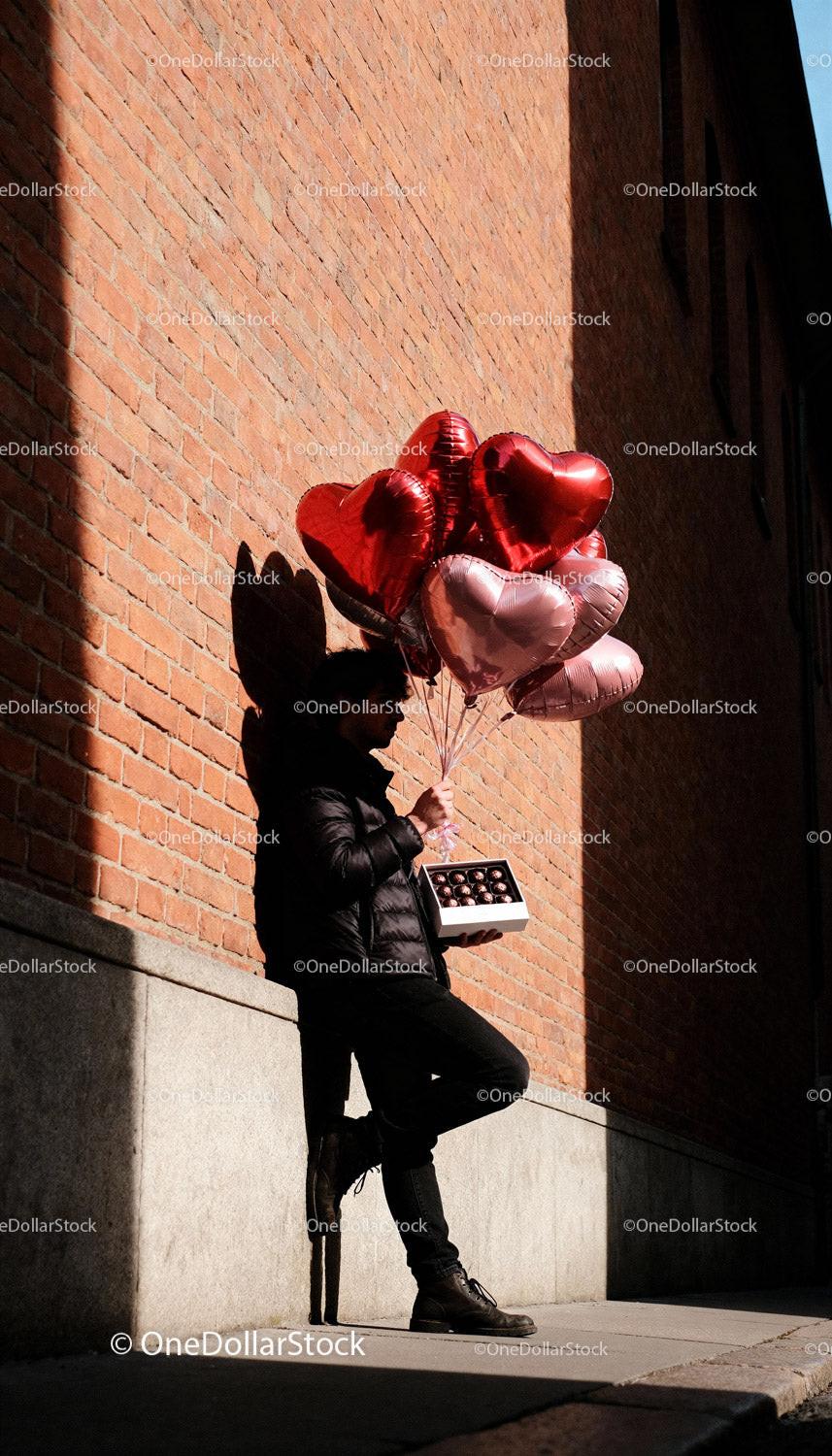 Man holding heart-shaped balloons and chocolates outdoors