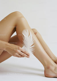 Elegant Woman's Legs with White Feather on Smooth Skin Art Photo