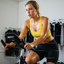 Focused Woman Exercising on Stationary Bike in Yellow Top