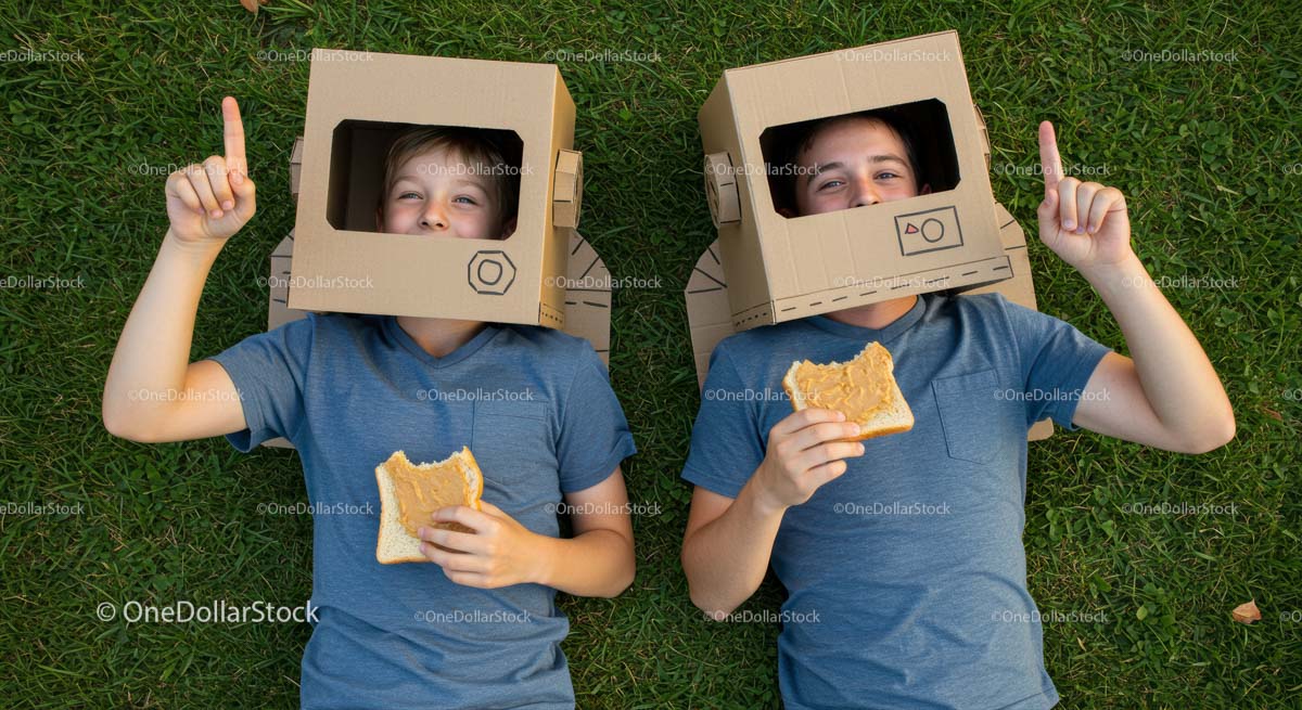 Children in Cardboard Helmets Enjoying Snacks on Grass
