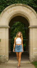 Young Woman in Denim Skirt and White Top at Stone Archway