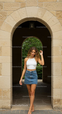 Fashionable Young Woman in Denim Skirt by Stone Archway