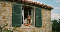 Woman Smiling Through Open Window of Rustic Stone House