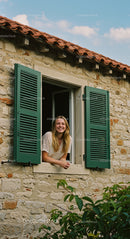 Smiling Woman by Open Window in Rustic Stone House