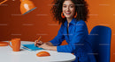 Smiling Woman in Blue Writing at Vibrant Orange Desk