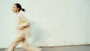 Dynamic Woman Running in Beige Outfit Against Minimalist Wall