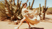 Woman in Flowing Beige Dress Dancing in Desert Landscape