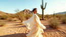 Woman in Flowing Dress Walking Through Desert at Sunset