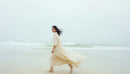 Woman in Flowing Beige Dress Walking by the Ocean