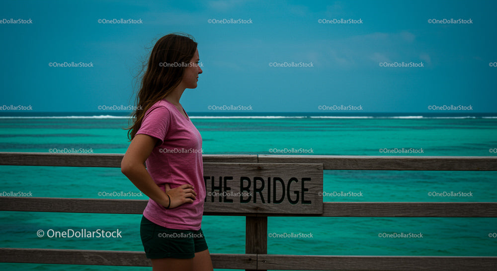 Woman Standing by Teal Ocean on Wooden Bridge