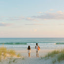 Two People Strolling on a Sandy Beach at Sunset