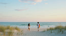 Two People Walking Towards Ocean at Tranquil Beach Sunset