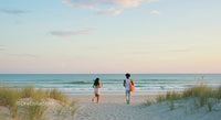 Two People Walking Towards Ocean at Tranquil Beach Sunset