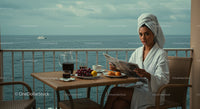 Woman Reading Newspaper on Seaside Balcony with Breakfast