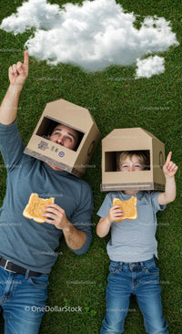 Father and Son Enjoy Creative Play on Grass with Cardboard Helmets