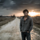 Man in Grey Hoodie on Country Road During Moody Sunset