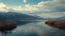 Scenic Lake with Mountains and Reeds Under Cloudy Sky