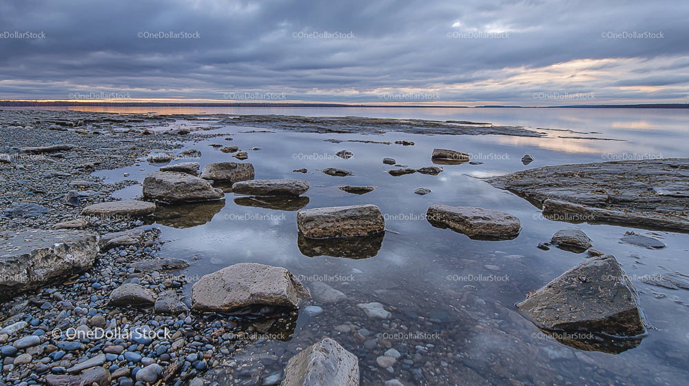 Rocky Shoreline Under Dramatic Cloudy Sky at Sunset