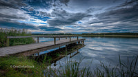 Wooden Pier Extending Over Calm Lake Under Dramatic Sky