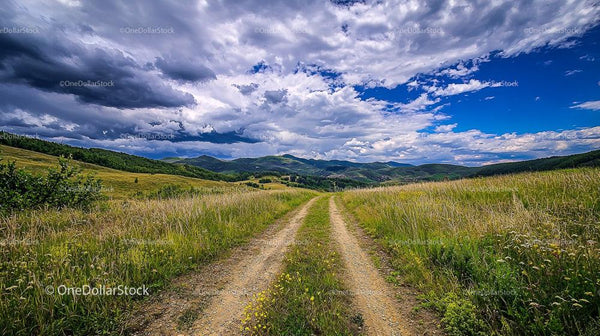 Dirt Road Leading Through the Rolling Hills Under Dramatic Skies