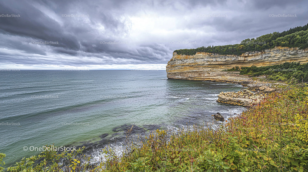 Dramatic Cliffside View with Stormy Skies and Calm Ocean