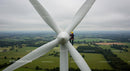 Technician Maintaining Wind Turbine Over Green Fields