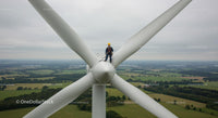 Maintenance Worker on Wind Turbine Overlooking Green Fields