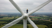 Engineer Inspecting Wind Turbine Above Green Fields
