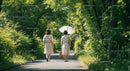 Two Women Walking with Parasol on Leafy Path