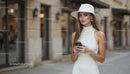 Elegant Woman in White Hat Strolling with Smartphone
