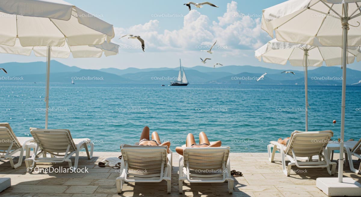 Relaxing on Sunbeds by the Blue Ocean with Sailing Boat