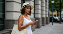 Woman in Straw Hat and White Dress Holding a Smartphone