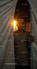 Contemplative Boy Peering Out from Tent at Sunset