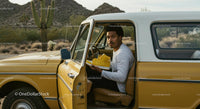 Young Man in Vintage Car Holding Yellow Sneakers in Desert
