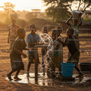 Children Playing at Water Pump in Rural Village at Sunset