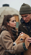 Couple in Winter Attire Caring for a Gentle Goat