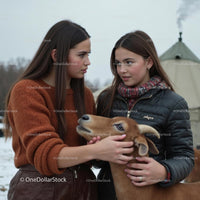Two Women Bonding with Brown Goat in Winter Setting
