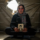 Somber Woman Holding a Photograph Inside a Refugee Tent