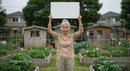 Elderly Woman Holding Sign in Lush Vegetable Garden