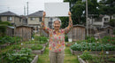 Senior Woman Holding Blank Sign in Urban Garden