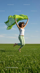 Joyful Woman Jumping with Green Scarf in Open Field