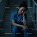 Exhausted Nurse in Blue Scrubs Sitting on Staircase