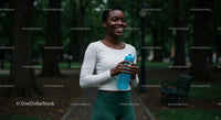 Smiling Woman Jogging in a Green Park with Water Bottle