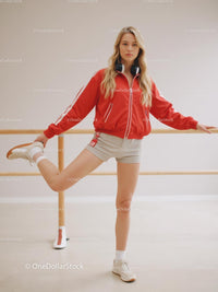 Young Woman in Red Jacket Stretching at Ballet Barre