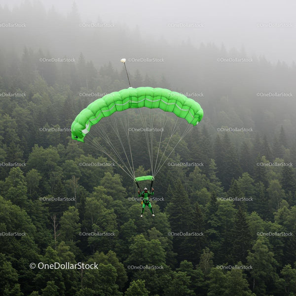 Skydiver with Green Parachute Over Misty Forest